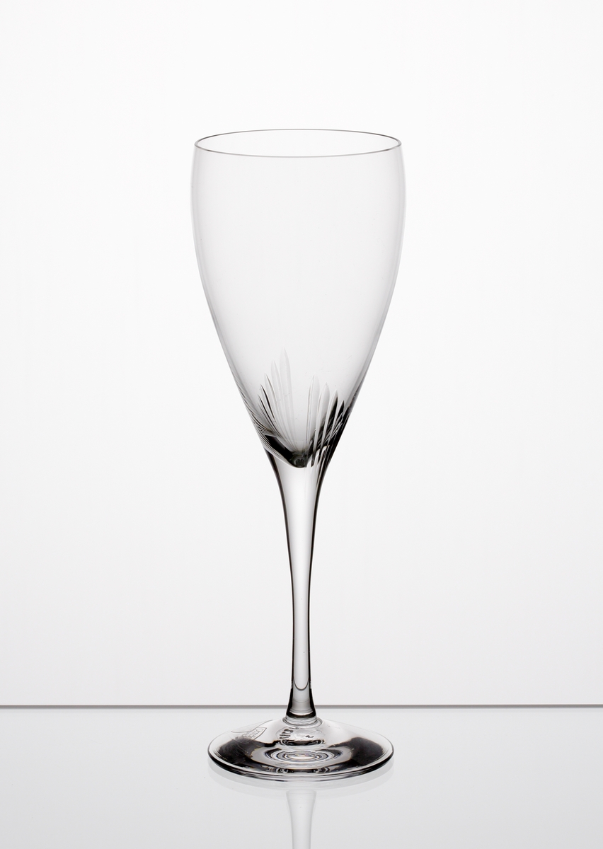 Formgiven av Erika Lagerbielke. Ölglas med nio plus nio stående skär placerade där skålen övergår i ben. Genomskinlig etikett med orre och text i silver.
