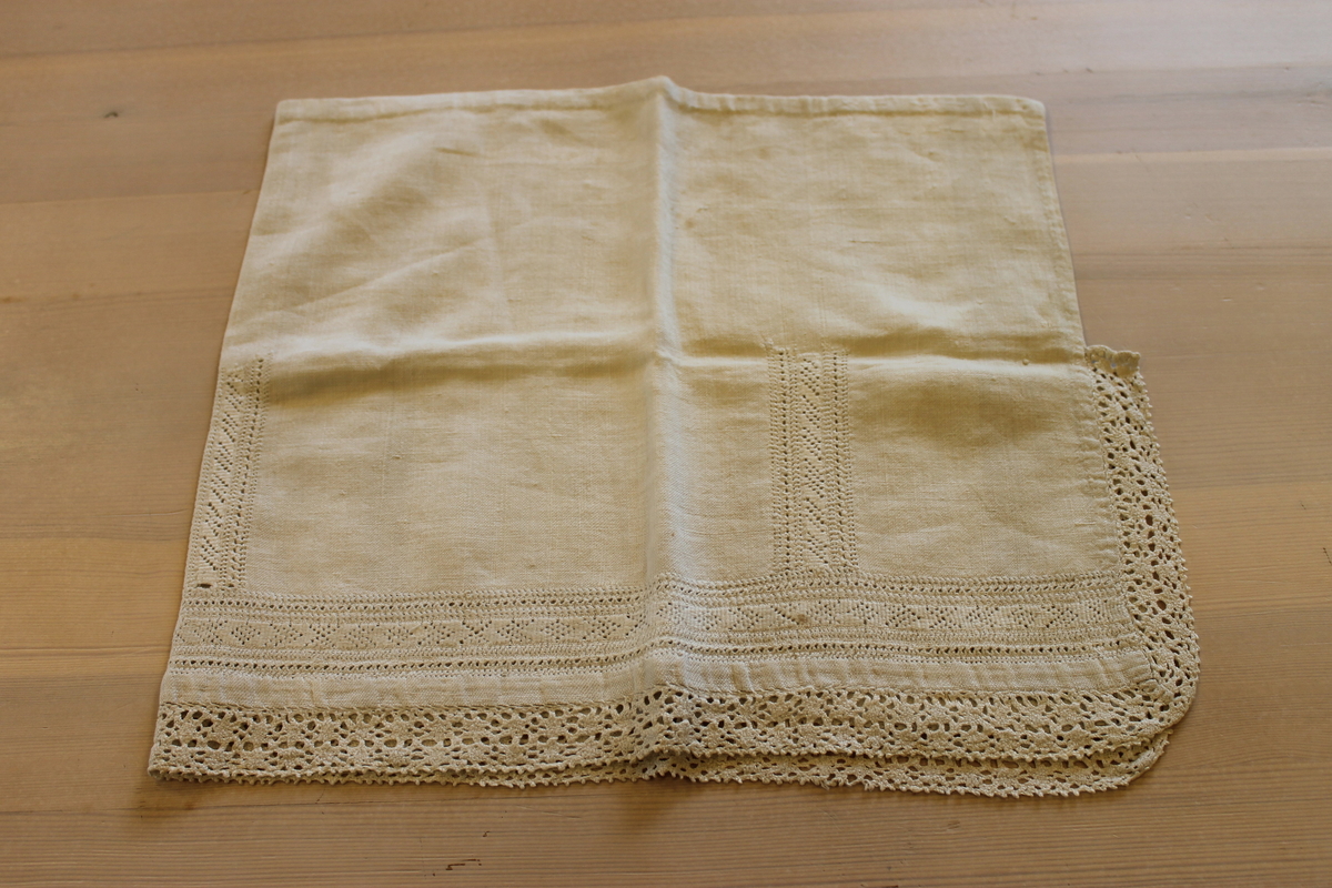 Rektangulært stykke lin (mål: 30,5 cm x 70cm ). Den ene halvdelen (brettet på langs) er rikt dekorert med tellesøm og kantet med bomullsblonde (trolig ikke håndlaget), mens den andre halvdelen, som blir brettet inn, er uten dekor