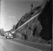 Rasberget vid länsgränsen 1961. En vattenkanon åker längst med en motorväg och har kanonen riktad mot en bergvägg. Vattnet träffar högt upp på berget och nedanför ligger rasmassor.