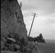 Rasberget vid länsgränsen 1961. En man står med ett spett vid en bergvägg. Runt honom finns rasmassor. Bakom honom står en elstolpe på sned.