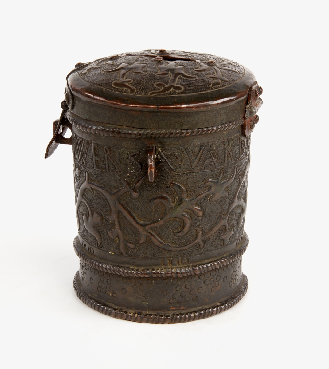 Sparbössa av koppar. Cylindrisk, med lock. Rikt dekorerad med ornament samt text: "Gifwer så varder eder givit 1666". På locket en skåra för myntinkast, på undersidan är sämskskinn fäst i en fastnitad kopparinsats. En ögla på var sida. Låsbygel mitt fram.