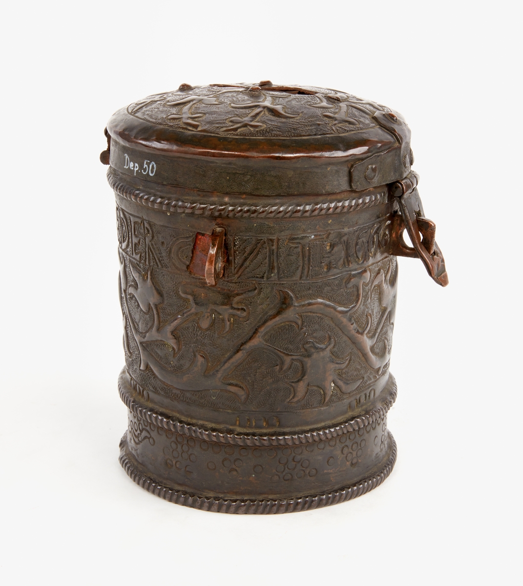 Sparbössa av koppar. Cylindrisk, med lock. Rikt dekorerad med ornament samt text: "Gifwer så varder eder givit 1666". På locket en skåra för myntinkast, på undersidan är sämskskinn fäst i en fastnitad kopparinsats. En ögla på var sida. Låsbygel mitt fram.