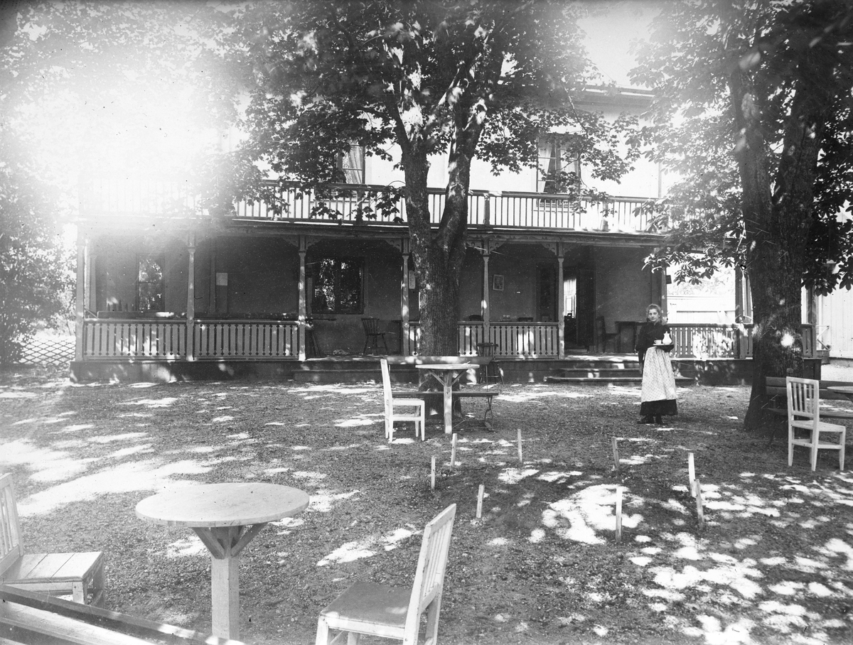 Nykvarns värdshus i för fotografen besvärande motljus. Apropå fotografen torde Folke Fromholtz varit för ung för att ha kunnat dokumentera värdshusets verksamhet som lades ned i början av 1900-talet. Möjligtvis pågick sporadisk servering vid värdshuset även efter den siste arrendatorens död, eller så har fotografiet annan upphovsperson än Fromholtz.