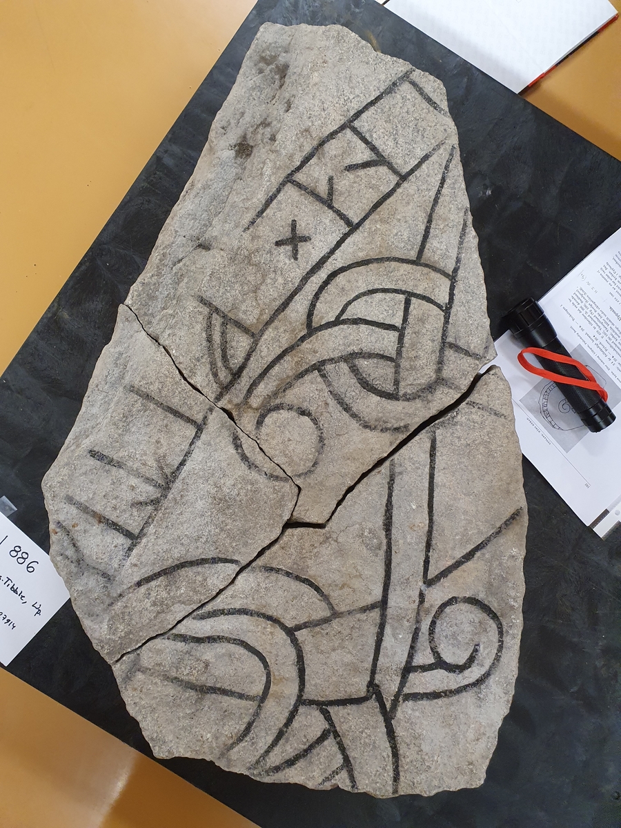 Runstensfragment med runslinga på två sidor, röd- och svartmålade. Inskrift  A: "...ina  x  fitiR...", "  B: "...ur  x  ...a x k...", (= ... denna (sten) efter...).