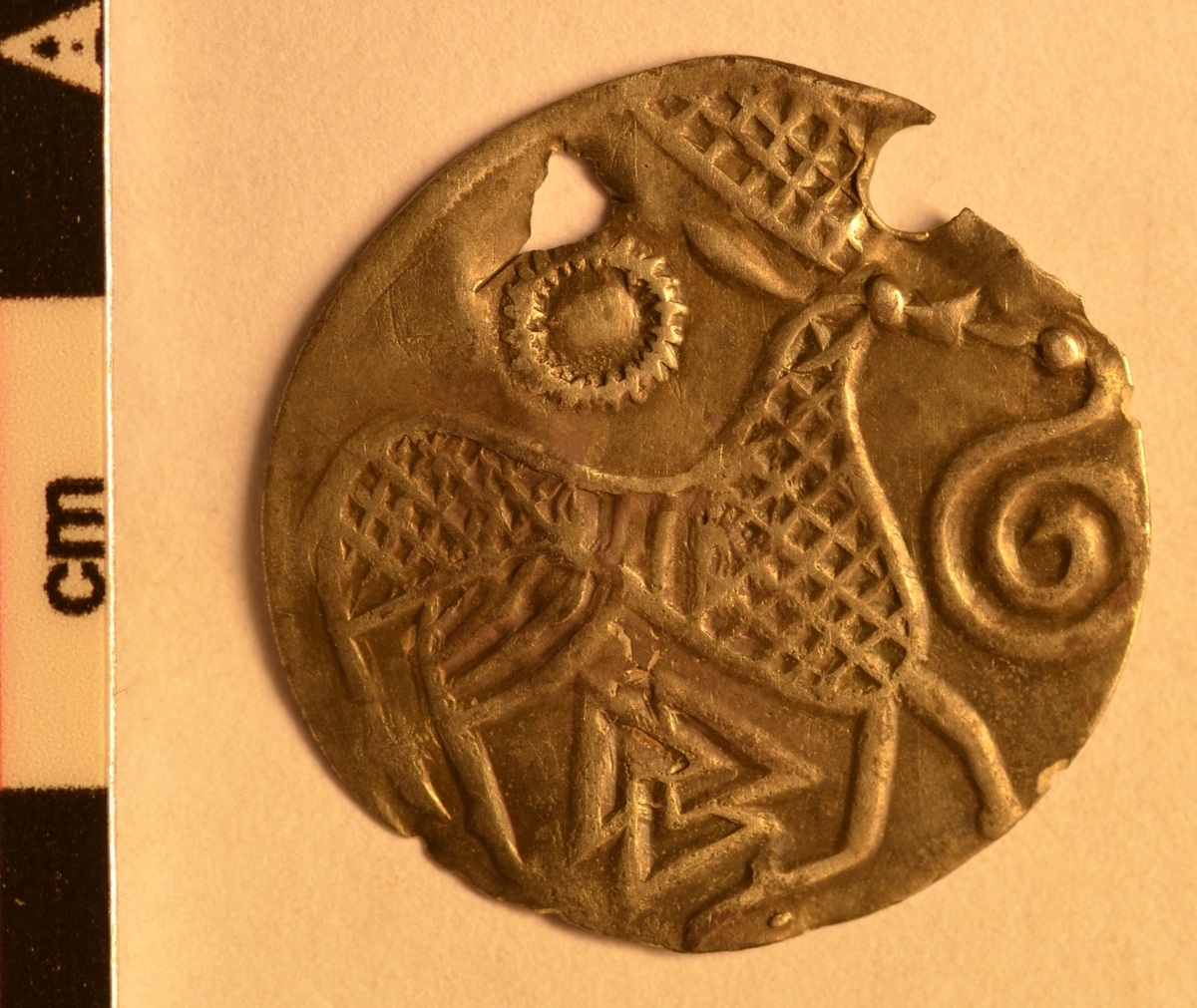 Motiv advers: Ansikt med stråler og bart. Fire mindre masker, to 8-tallsymbol og to slanger i ring rundt. 

Motiv revers: Hjort som vender framover, slange foran mulen, solsymbol bak og trikvetra symbol under. 