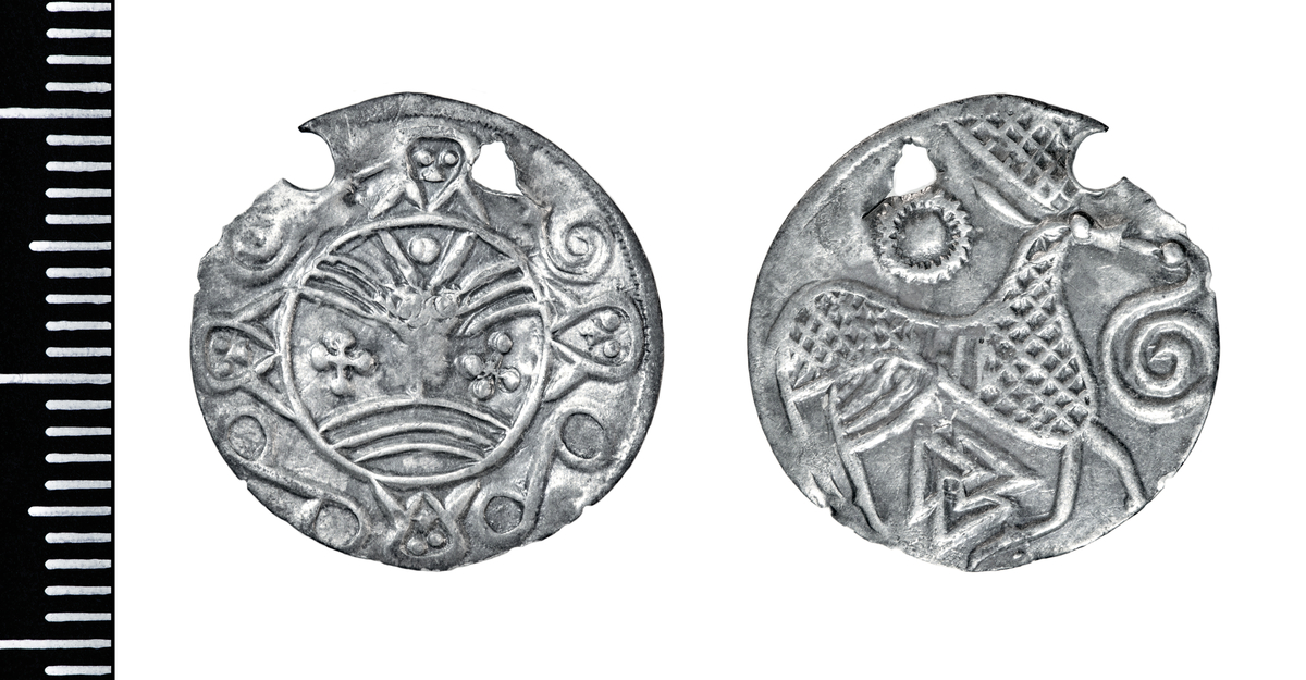 Motiv advers: Ansikt med stråler og bart. Fire mindre masker, to 8-tallsymbol og to slanger i ring rundt. 

Motiv revers: Hjort som vender framover, slange foran mulen, solsymbol bak og trikvetra symbol under. 