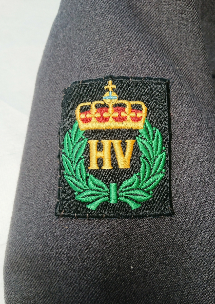 Merkene for Norges Lotteforbund og Heimevernet er fastsydd på henholdsvis venstre og høyre jakkeerme. Jakka har fôr.