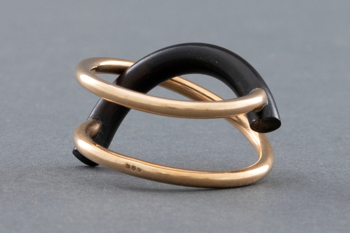 Ring laget av gulltråd med form som en åpen spiral tvunnet 1 1/2 gang. Et halvsirkelformet gummistykke, litt tykkere enn gulltråden er festet til hver ende av gullspiralen. Gummistykket blir slik stående på tvers av denne.