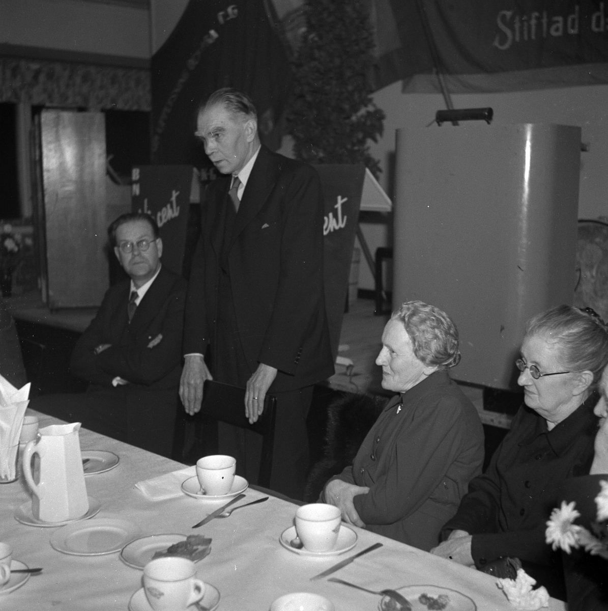 Alingsås Arbetarkommun firar 40 år, 1947, i Folkets hus. Stadsfullmäktiges ordförande H.M. Enander står upp och talar. Bredvid sitter Anna Enander.