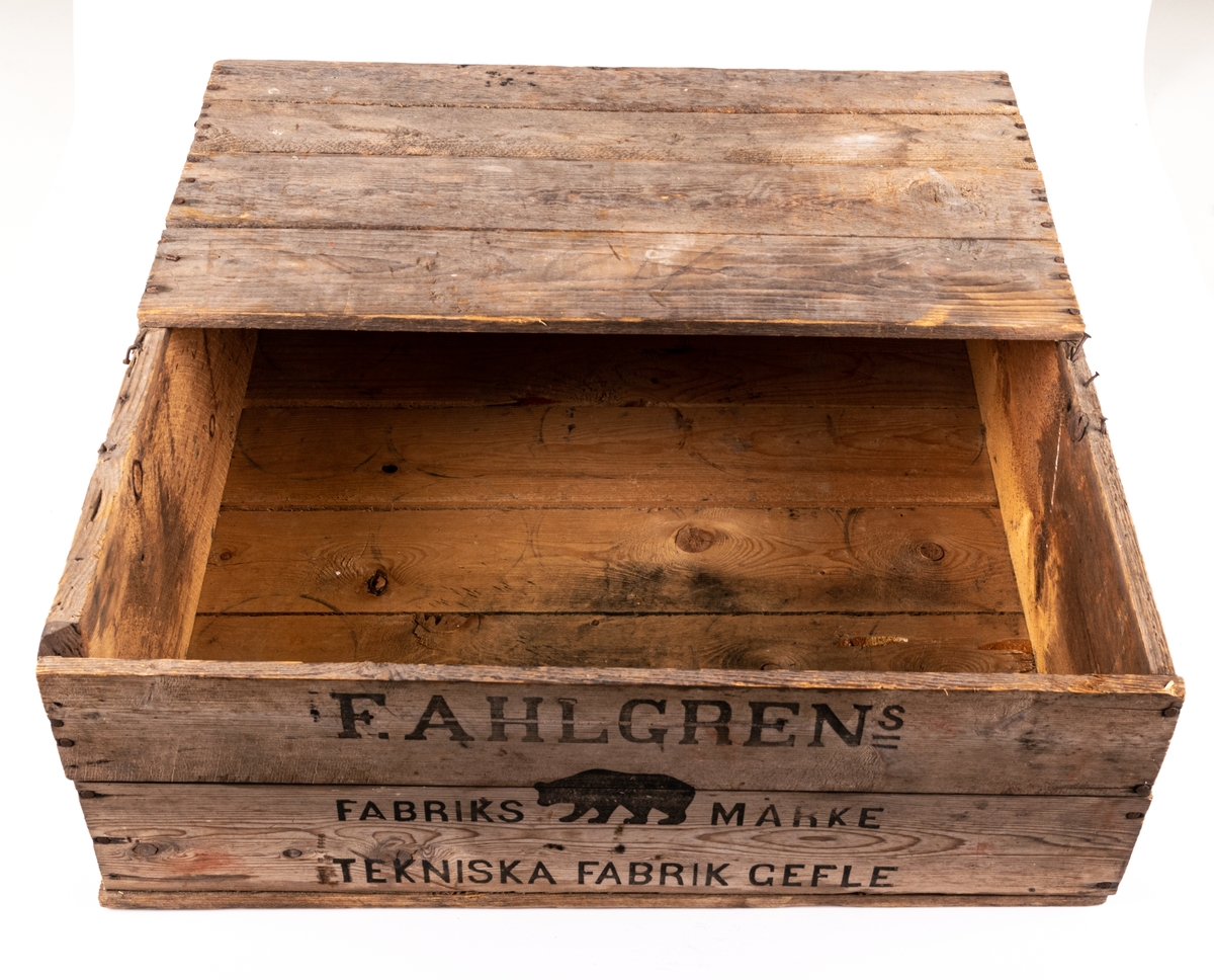 Trälåda, snickrad av ohyvlade brädlappar, spikad. Locket uppbrutet. Stämplar och påskrift på sidorna: "F. Ahlgrens Tekniska Fabrik".