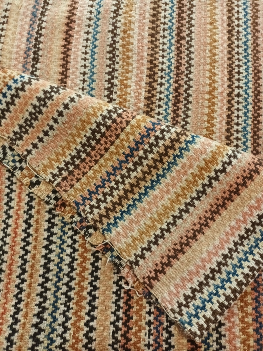 Teppe i krokbragd i mange fargar. Renning: 26/10 cm. tvunnet lintråd. Innslag: 2trds ullgarn. Teppet er skjøtt på midten, og bordane møtes tilfeldig i skøyten.