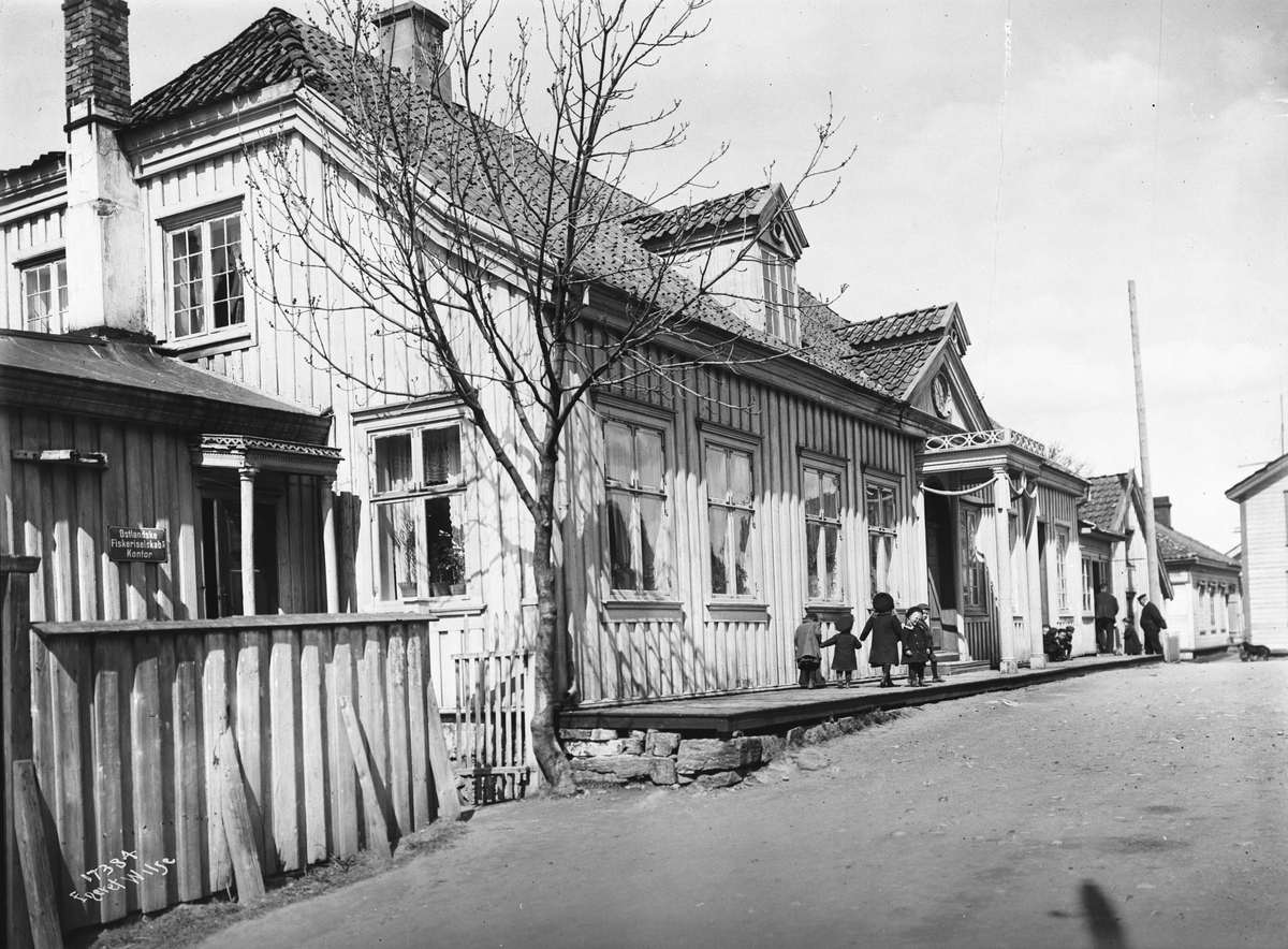 Bygning i Langesund med små barn gående på plattingen og Østlandske Fiskeriselskabs Kontor ved siden av, 1915.