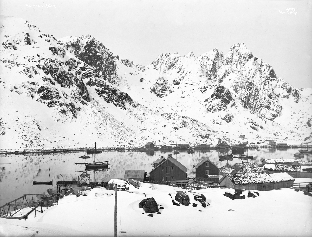 Fiskevær med fortøyde fiskebåter og fjell dekket av snø i bakgrunnen i Ballstad på Vestvågøy april 1917.