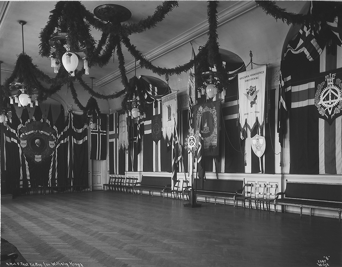 Haandværk- og Industriforeningen har pyntet til fest i anledning dekorasjons- og teatermaler Wilhelm Kroghs 80 årsdag.
80-års dag. Fotografert 1909.