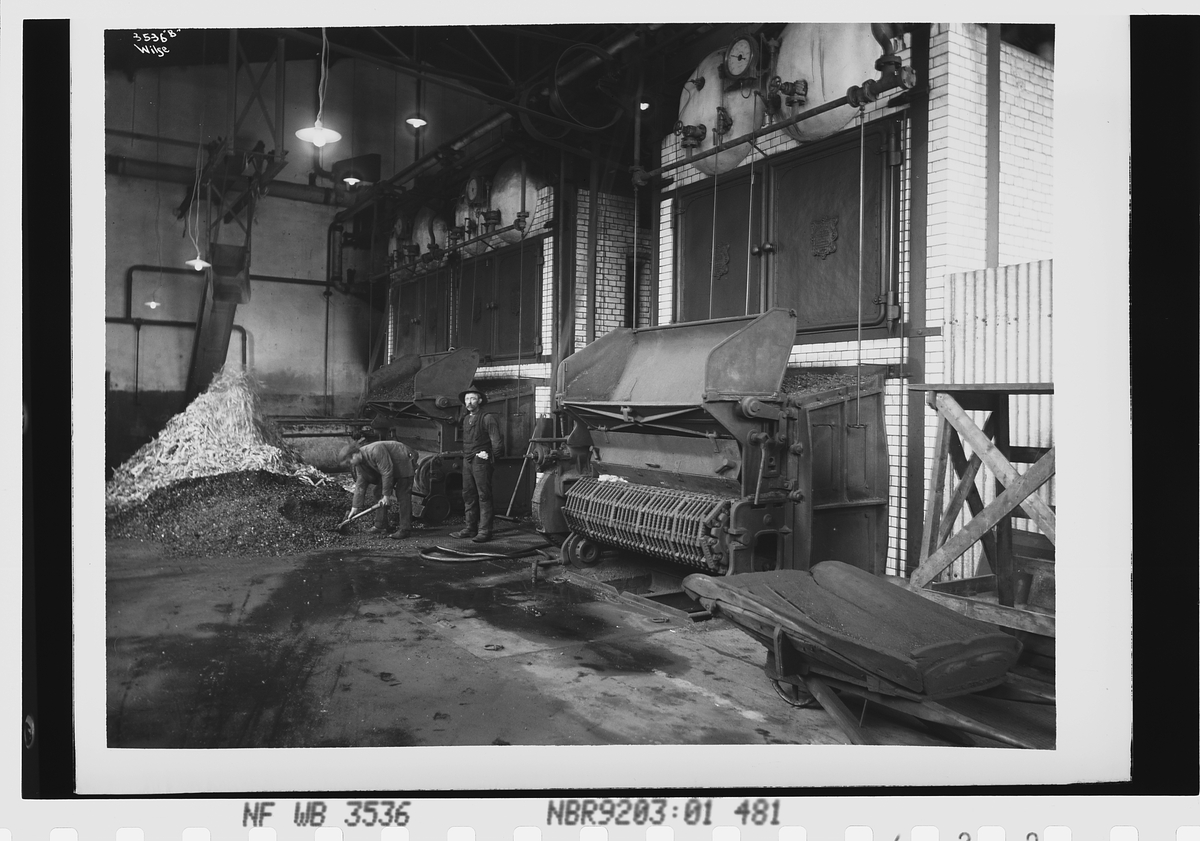 To ansatte arbeider i fyrrommet på Lillestrøm Cellulosefabrikk AS. Det brukes både sagflis og kull. Fotografert 1912.