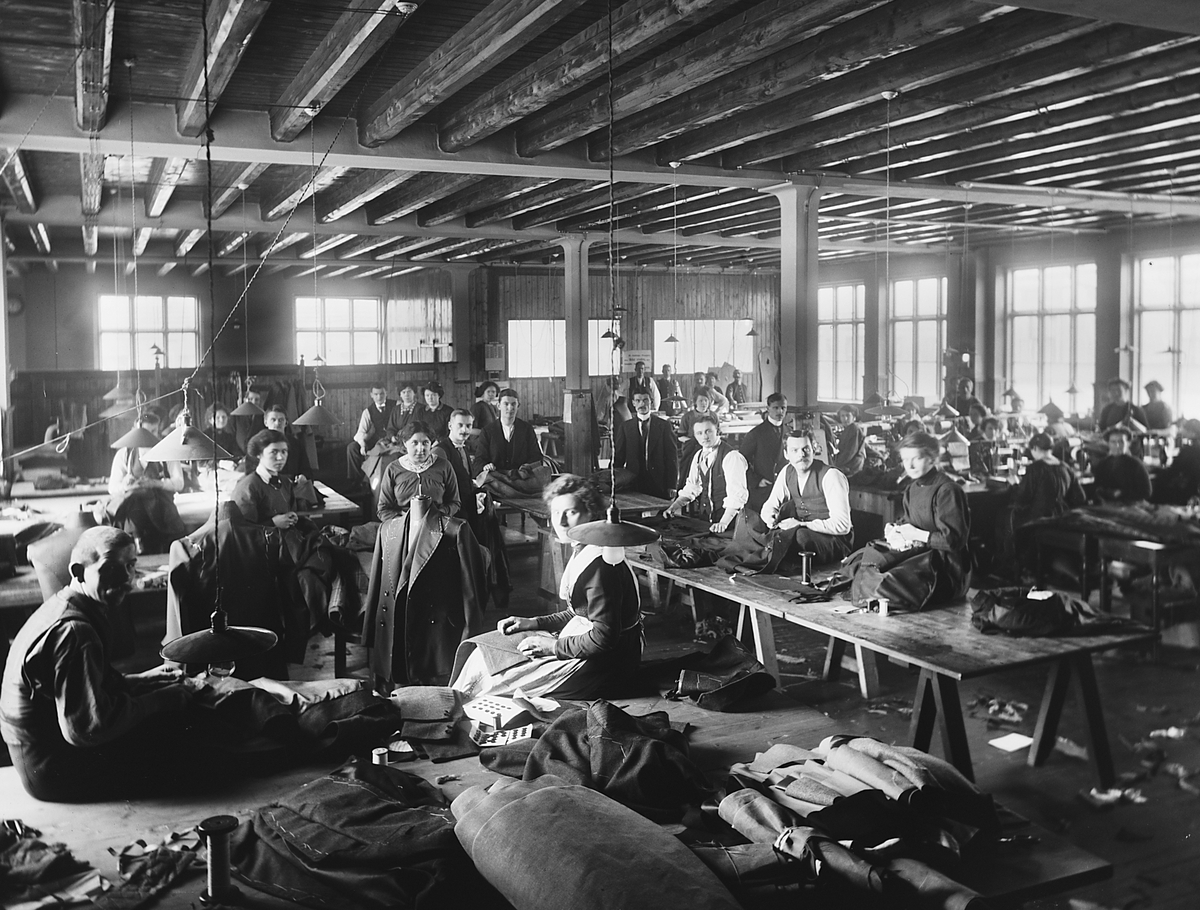Herkules Konfeksjonsfabrikk.  Arbeiderne sitter i skredderstilling på bordene og syr.  Ingen maskiner, men godt håndverk.