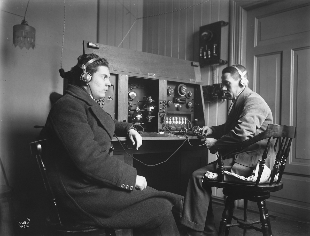 To yngre herrer lytter til radio, antatt yrkesspesialister innenfor telefon og telegraf.