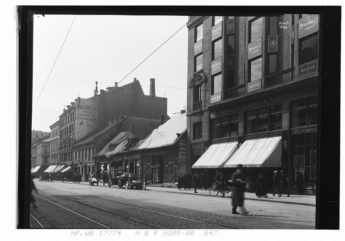 Butikker, kontorer, bil og fotgjengere i Storgata. Fotografert 1924.