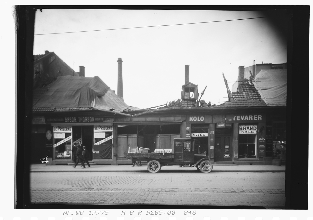 Bil står utenfor en nedbrent butikk i Storgata. Fotograftert 1924.