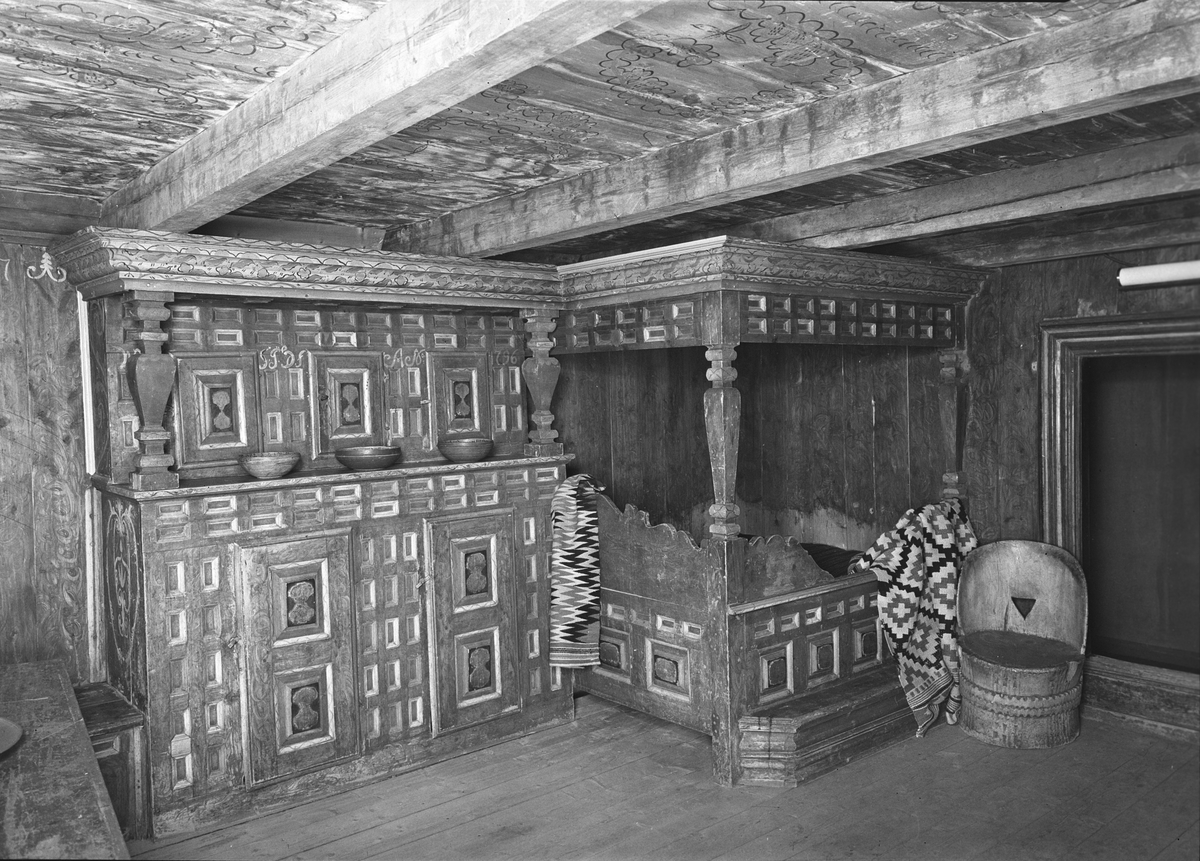 Interiør Damm & Sønn, Fellandstua NF.627, Folkemuseet.  Framskap, seng, kubbestol og åkle. Vakkert utskåret vevet.