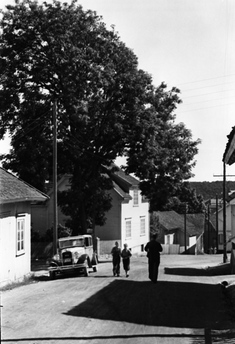 Gatebilde fra Langesund, trevillaer, personbil parkert i veikanten, 2 gutter og en mann på vei ned bakken.