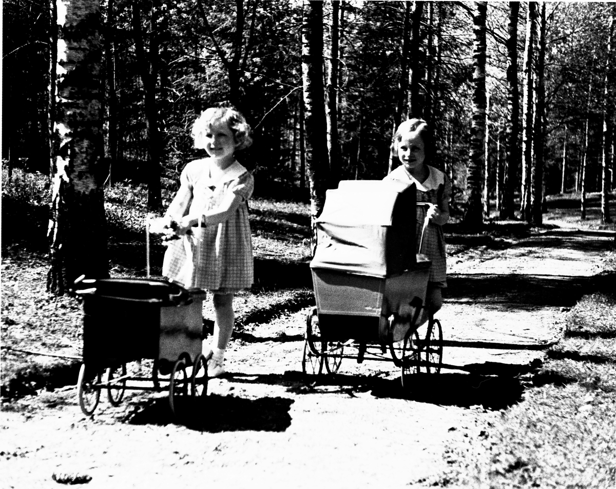 Kongefamiliens små prinsesser Ragnhild og Astrid ute med dukkevognene sine i solen på Skaugum.