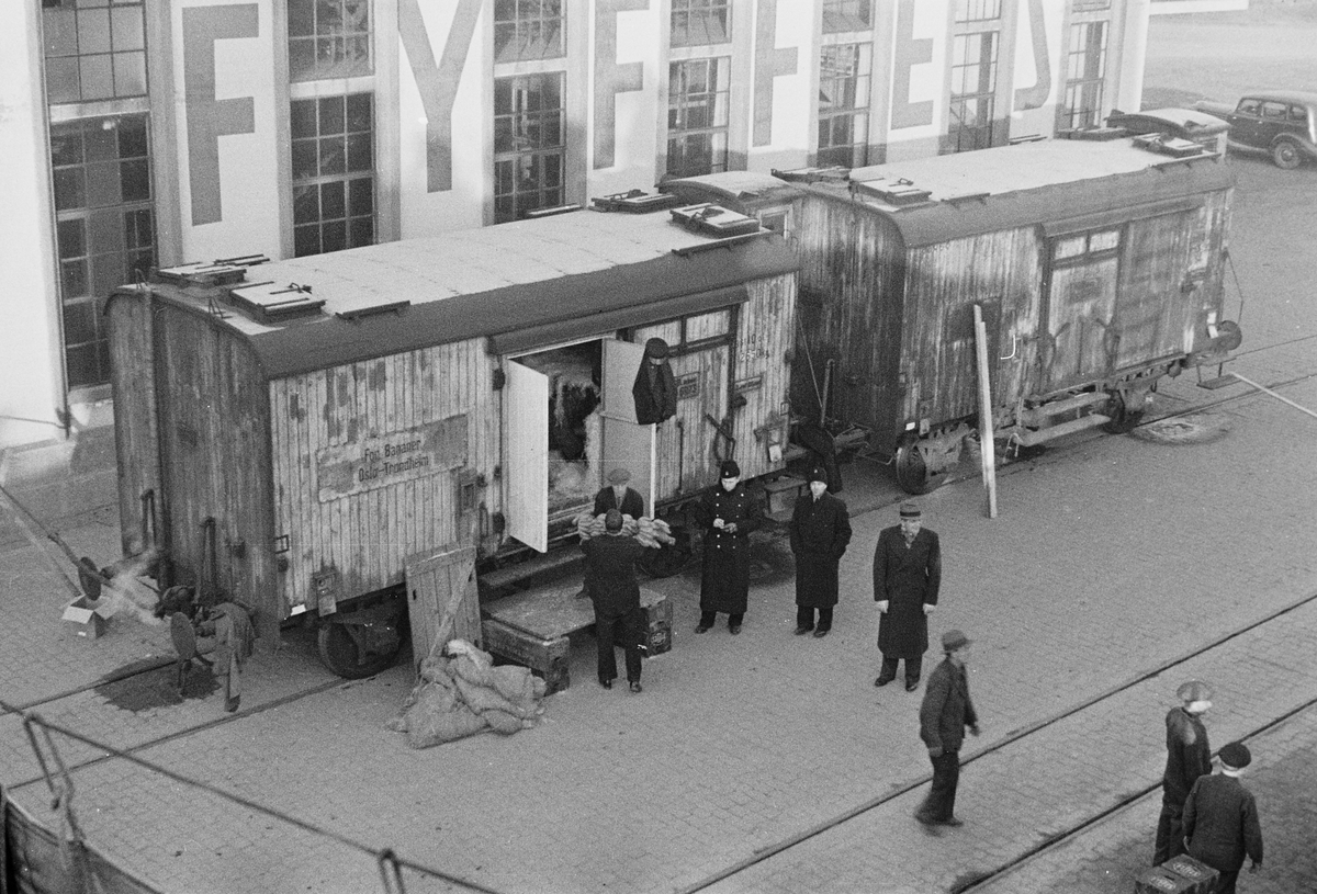 Oslo Havn, lessing og lossing fra to vogner på bryggen.  Kjøp og salg, politi på plass.  I bakgrunnen større lagerbygning
