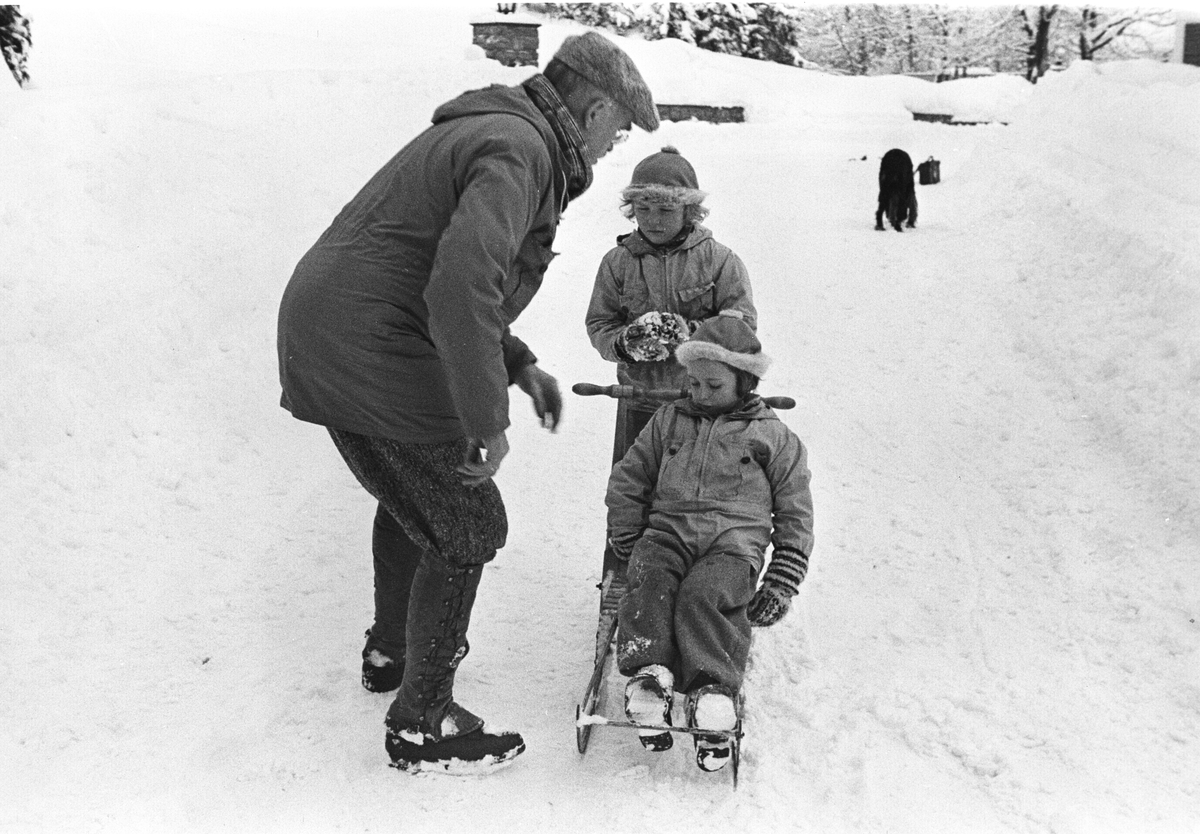 Prinsessene Ragnhild og Astrid på sparketur i vinterværet. Mannen som passer på, ser ut til å ha noen gode råd til barna.  Hunden er også med på turen.