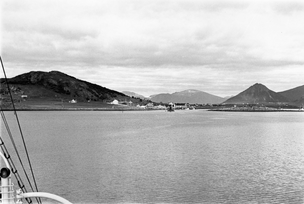 Fra båten ser vi mot bebyggelsen og fjellene i bakgrunnen.  Blank sjø.