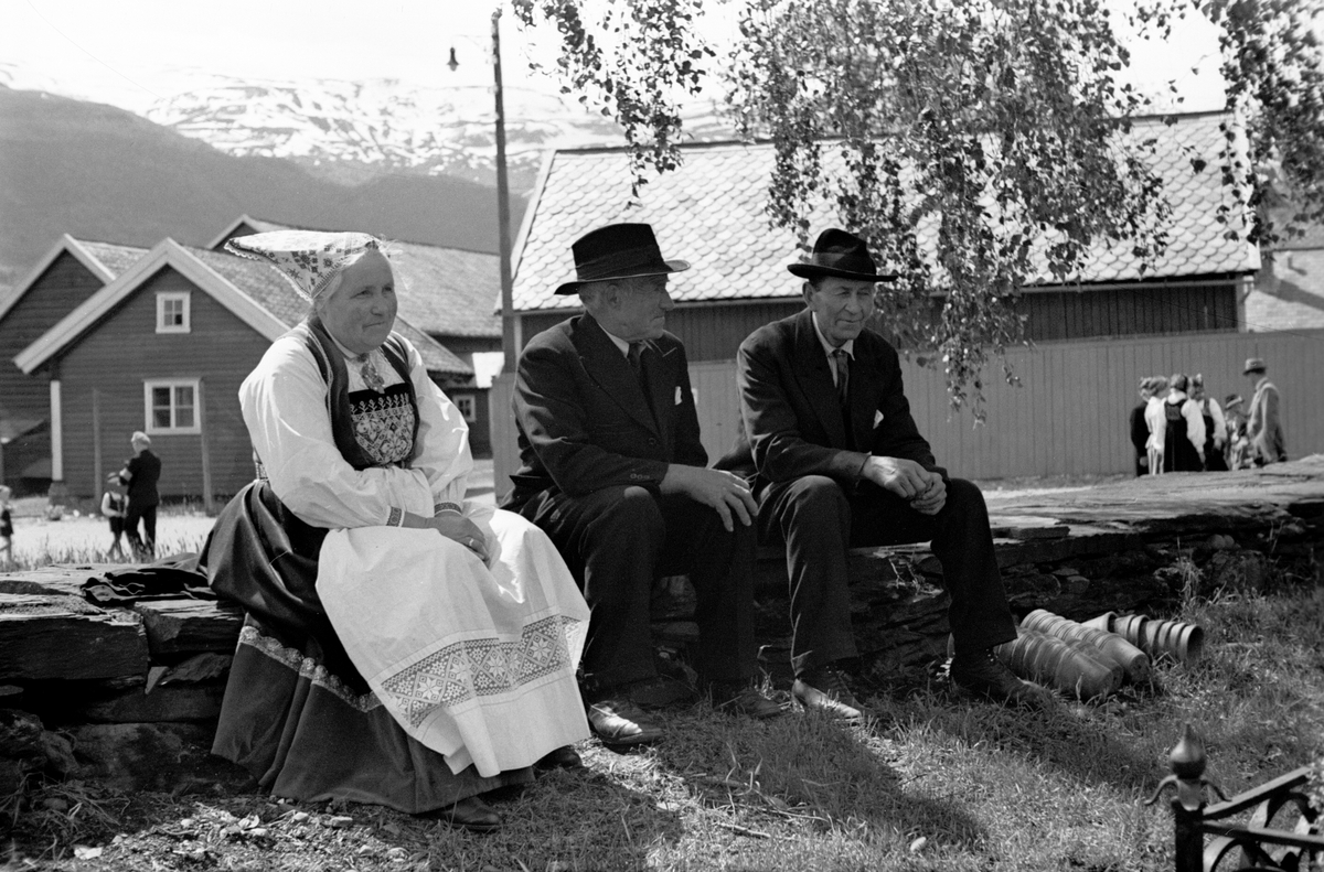 To menn og en kvinne alle festkledd, tar en pust i bakken på kirkebakken.