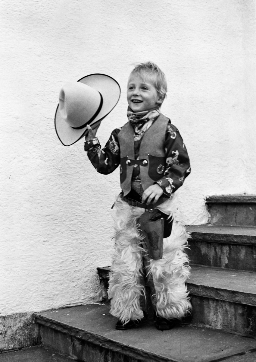 Arveprinsen står i trappen i fullt cowboyutstyr, tydelig fornøyd med påkledningen.