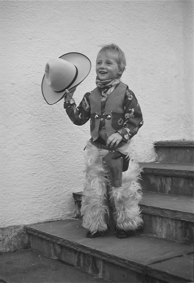 Arveprinsen står i trappen i fullt cowboyutstyr, tydelig fornøyd med påkledningen.