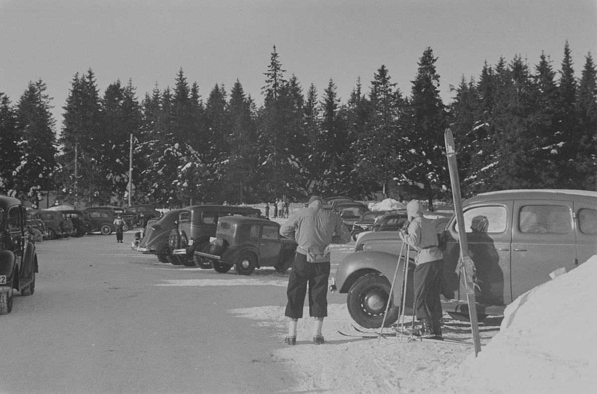 Biler og skiturister på parkeringsplass anntatt på Frognerseteren, Holmenkollen, Oslo. Fotografert 1940.