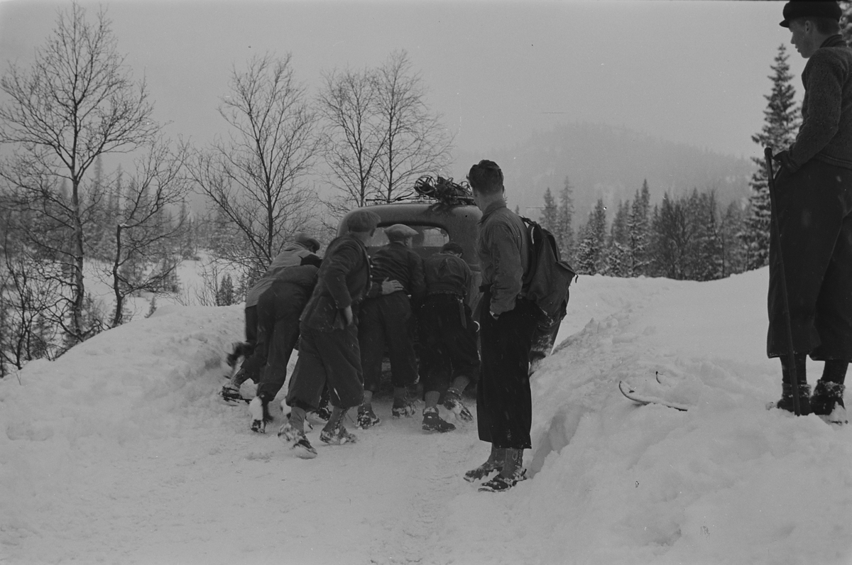 Bil på antatt på påsketur får skyvehjelp på vinterføre. Fotografert 1940.