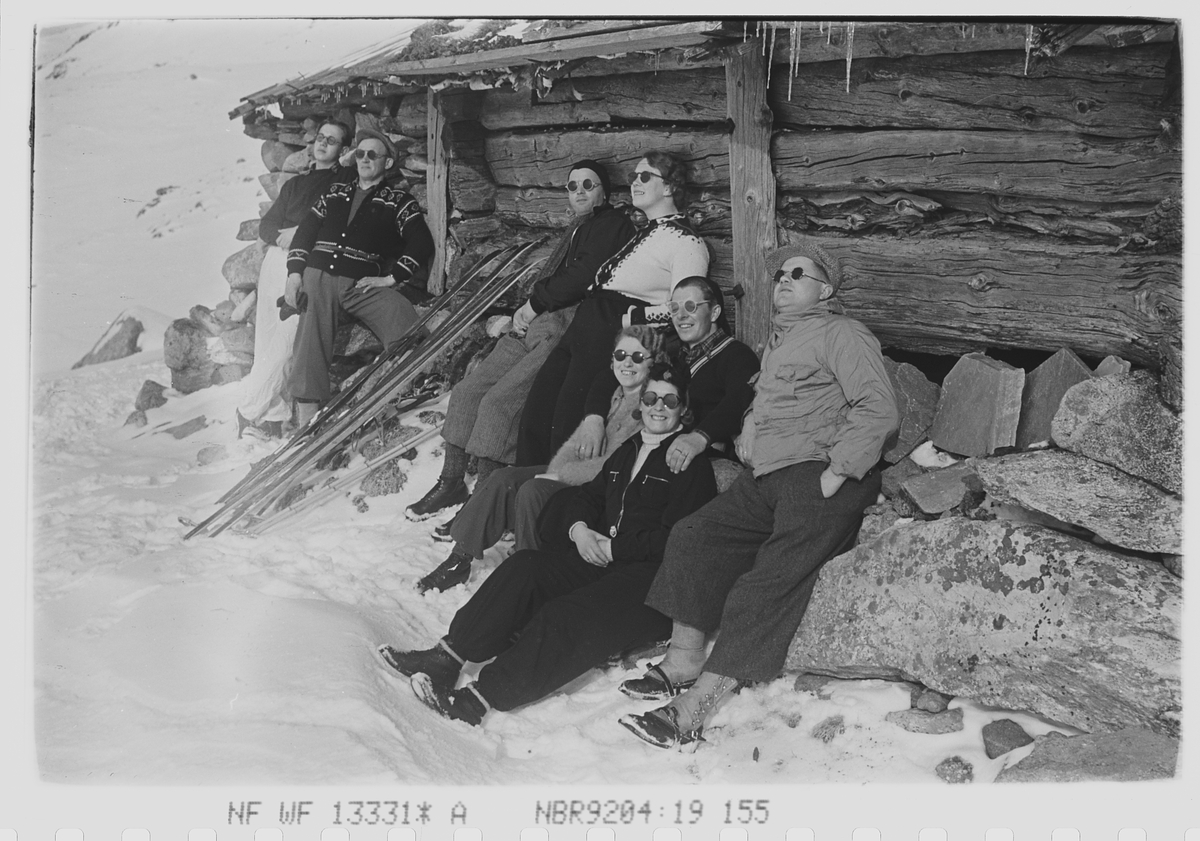 Åtte påsketurister soler seg ved seterbygning i fjellheimen. Fotografert 1940.