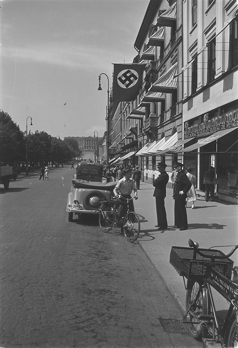 Uniformerte menn under nazistflagg med hakekors på Karl Johans gate, Oslo. Fotografert 1940.