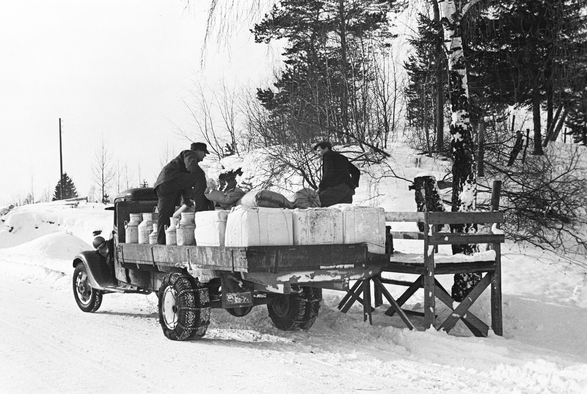 Menn på lasteplanet til melkebilen med melkespann og cellulosefor., ved en melkerampe. Haugsbygda, Ringerike. Fotografert 1941.