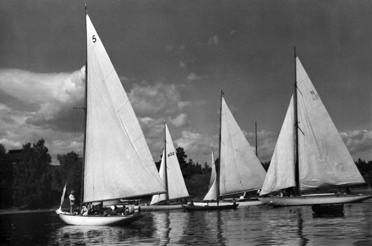 Regatta i vindstille. Blank sjø og store båter i tillegg til mannskapet som ønsker seg litt vind i seilene.