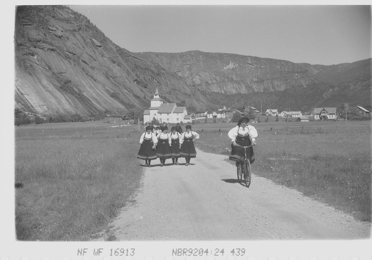 Valle kirke i bakgrunnen, bunadskledde kvinner på hjemvei fra kirken.