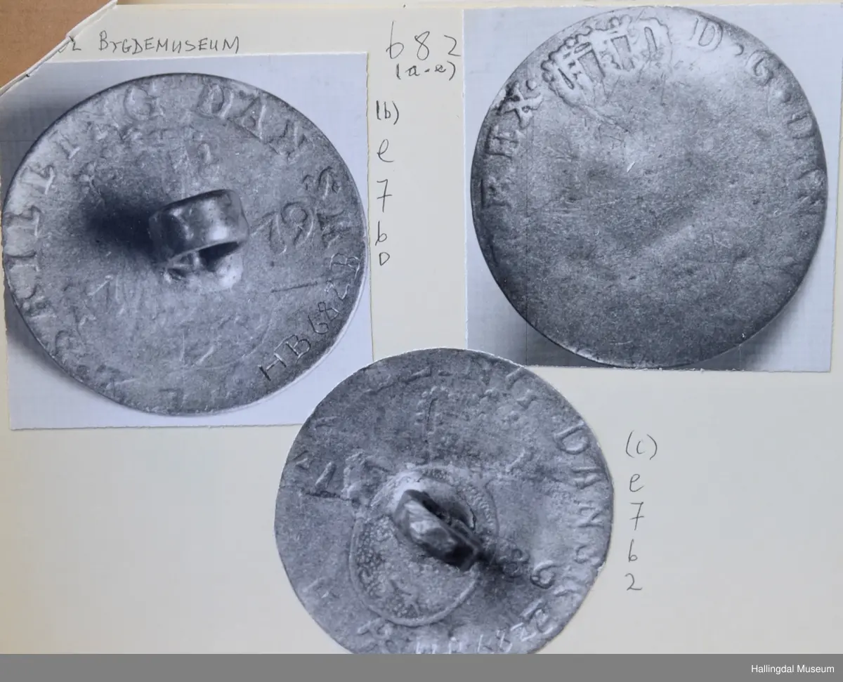 Myntknapp, sølv. Laget av mynt. 
a) Baksiden merket med det kronede dobbeltmonogram F.4. Framsiden med: "..Skilling danske 1705".
b) Baksiden merket: "2 skilling danske 1779" samt våpenmerke. Framsiden sterkt avslitt.
c) Baksiden merke: "2 skilling danske 1786", samt våpenmerke. Framsiden sterkt avslitt.
d) Baksiden merket: "2 skilling danske 1787", samt våpenmerke. På framsiden rester av kronet C7.
e) Baksiden merket med kronet C7 (?), framsiden helt avslitt.
R.B.S.