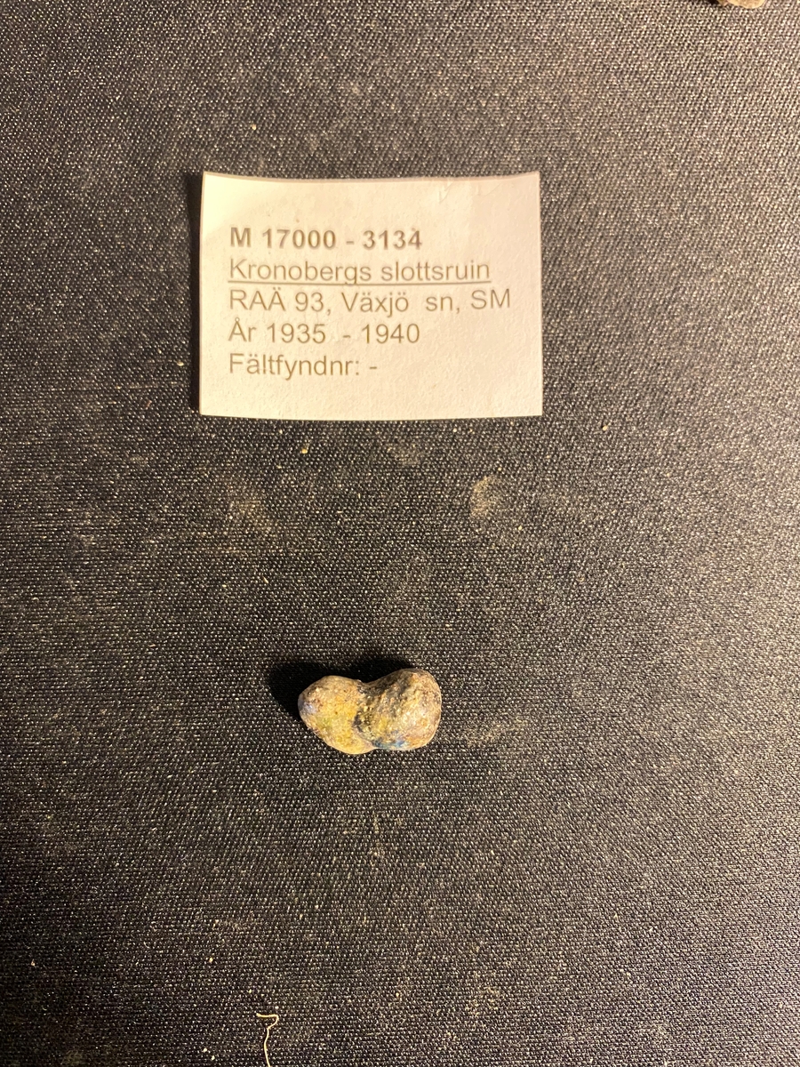 Ugnsrester av bränd lera samt ett tätt, finkornigt och strimmigt stenmaterial, sannolikt glimmerskiffer. Flera av delarna har ett tunt lager av ljust turkos glasmassa på sidorna. Även ett bönformat glasdropp. Liknande glasdroppar  (Se ex. M 17000-3172) och ugnsfragment återfinns ofta vid tidighistoriska glashyttor.