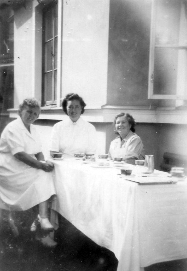 Personal på Kustsanatoriet Apelviken dricker te utomhus i solen intill en husfasad. Kvinnan i mitten kan vara Greta Österberg, gift med Olof Österberg (ej bekräftat).