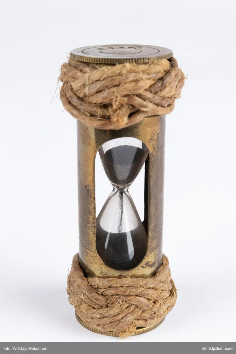 Lite timeglass i glass og metall og tau i makrame i begge ender. Tyrkerknop.