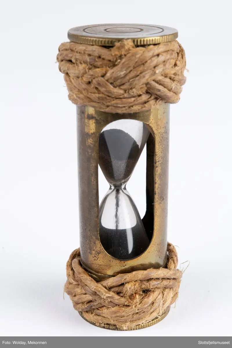 Lite timeglass i glass og metall og tau i makrame i begge ender. Tyrkerknop.