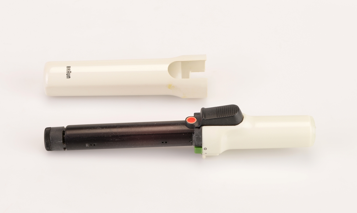 En krølltang av typen "Braun independent curler" i originalemballasje. Esken er av papp og har tekst/illustrasjoner på alle sider. Det er blant annet flere fotografier av krølltangen asmt fotografier som visr at den tar liten plass og at man kan fikse håret når som helst og hvor som helst. Esken åpnes på toppen og henger fast i bakkanten på esken. På undersiden av lokket er det informasjon og illustrasjoner som informerer om bruk av krølltangen. I eskdedelen er det et "utstillingsvindu" delvis dekket med plast. Krølltangen ligger i en burgunderfarget plastinnsats som er formet etter tangens deler. Krølltangen er to deler og laget av hvit plast og svart metall. på tangens håndtak er det en knapp somtrykkes ned og da går en del av tangen opp lsik at man kan rulle håret opp. Til hører det også til en beskyttelseshette av hvit plast. Gassbeholderen mangler.