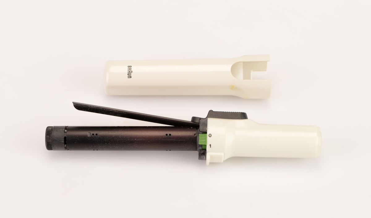 En krølltang av typen "Braun independent curler" i originalemballasje. Esken er av papp og har tekst/illustrasjoner på alle sider. Det er blant annet flere fotografier av krølltangen asmt fotografier som visr at den tar liten plass og at man kan fikse håret når som helst og hvor som helst. Esken åpnes på toppen og henger fast i bakkanten på esken. På undersiden av lokket er det informasjon og illustrasjoner som informerer om bruk av krølltangen. I eskdedelen er det et "utstillingsvindu" delvis dekket med plast. Krølltangen ligger i en burgunderfarget plastinnsats som er formet etter tangens deler. Krølltangen er to deler og laget av hvit plast og svart metall. på tangens håndtak er det en knapp somtrykkes ned og da går en del av tangen opp lsik at man kan rulle håret opp. Til hører det også til en beskyttelseshette av hvit plast. Gassbeholderen mangler.