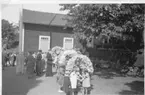 En grupp barn med blomsterbågar står på en bakgård.