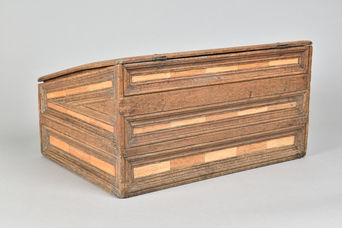 Skrin tillverkat i ek, med rik intarsia av två andra träslag. Rektangulär till formen med pulpetlock. Locket med profilerad och centrerad spegel. Framsida med nyckelhål och nyckelskylt, samt två lådor med draghandtag av mässing. Lådorna går att låsa från skrinets insida med hjälp av två träpluggar. Insidan av skåpet försedd med avsats för placering av skrivredskap samt tre mindre lådor med dragknoppar. 