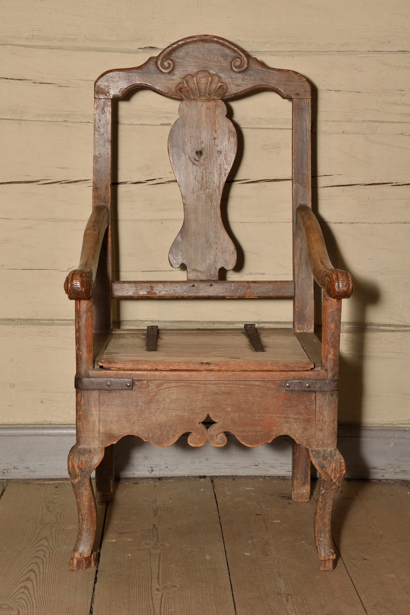 Stol tillverkad i björk och furu, rokokostil. Rak, delvis genombruten rygg med balusterformad ryggbricka. Krönet av stolsryggen med skuren ornering i form av voluter och snäcka. Lätt svängda armlän med dekorativt skurna avslut i form av voluter och akantusblad. Rak ostoppad sits i två delar, överst lucka med järnbeslag vilken går att fälla upp, under en sits med utskuret hål för placering av nattkärl. Bred sarg med skuren dekor i böljande vågmönster, samt var sida med genombrutet stjärnformat hål. Stolen vilar på fyra ben, de bakre enkla och raka, och de främre lätt svängda med skuren mussla.