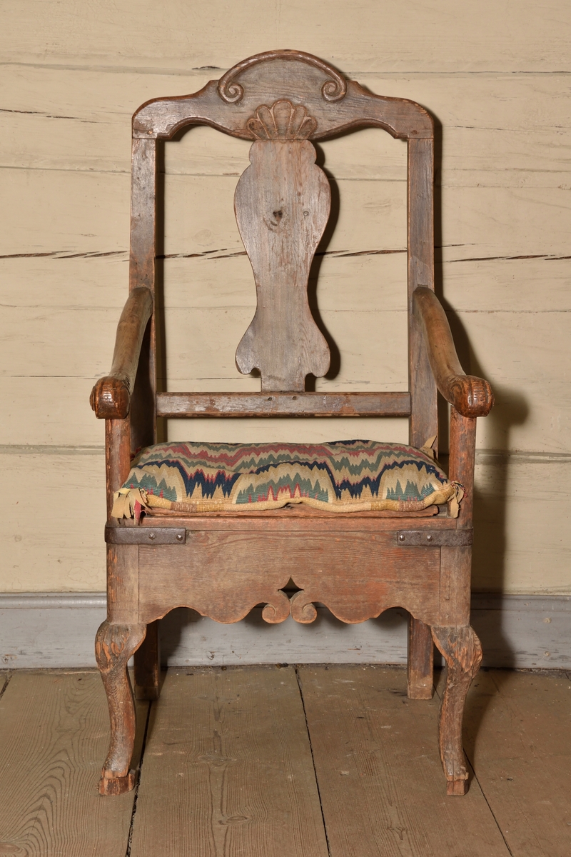 Stol tillverkad i björk och furu, rokokostil. Rak, delvis genombruten rygg med balusterformad ryggbricka. Krönet av stolsryggen med skuren ornering i form av voluter och snäcka. Lätt svängda armlän med dekorativt skurna avslut i form av voluter och akantusblad. Rak ostoppad sits i två delar, överst lucka med järnbeslag vilken går att fälla upp, under en sits med utskuret hål för placering av nattkärl. Bred sarg med skuren dekor i böljande vågmönster, samt var sida med genombrutet stjärnformat hål. Stolen vilar på fyra ben, de bakre enkla och raka, och de främre lätt svängda med skuren mussla.